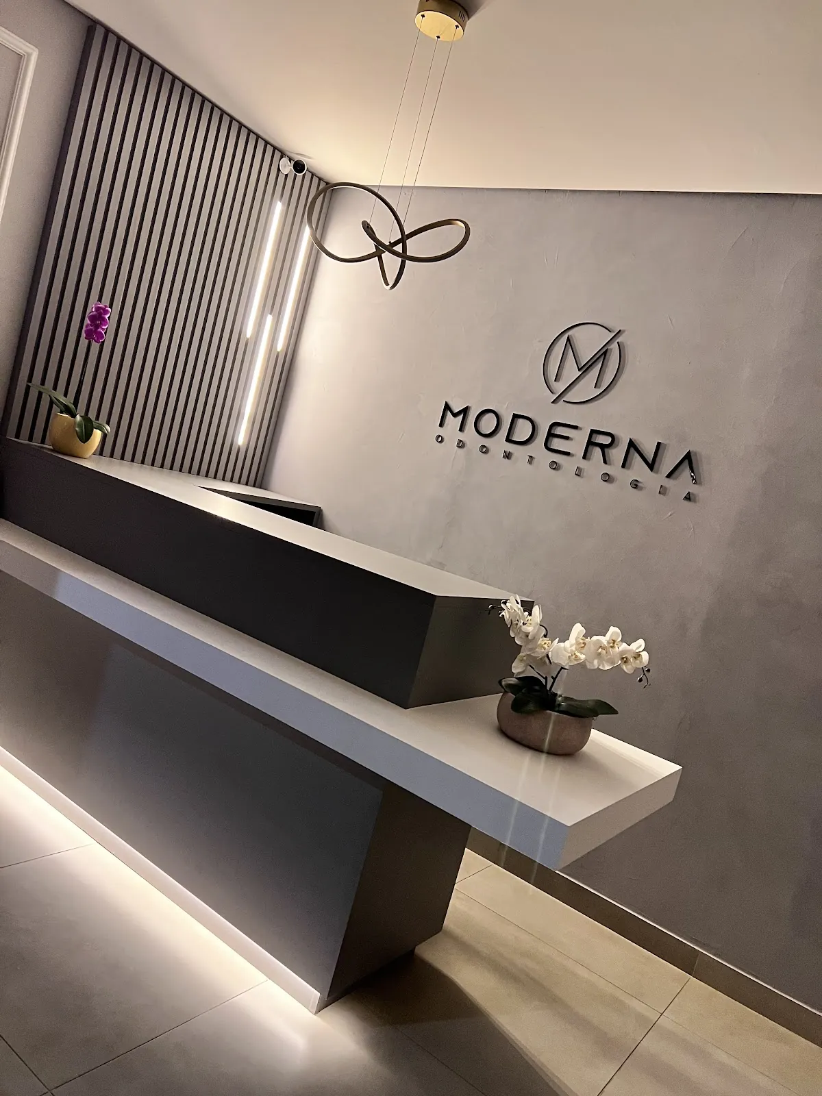 Recepção da Moderna Odontologia, com balcão branco, parede de cimento queimado e o logotipo da clínica